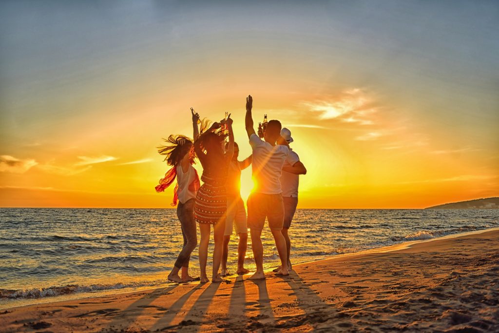 group of happy young people dancing at the beach on beautiful summer sunset.